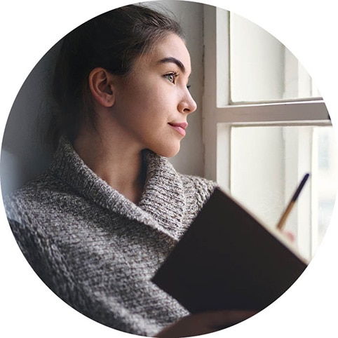 Person sitting on a windowsill and writing in a notebook